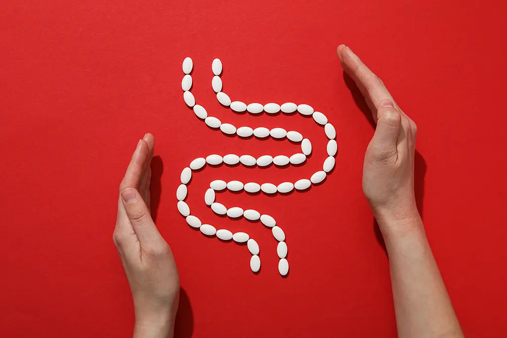White pills arranged in a zigzag pattern between two hands against a red background, symbolizing intestinal health.