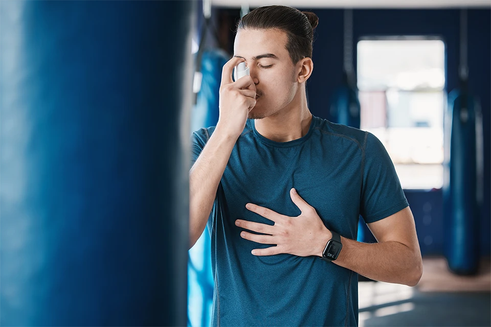Man experiencing discomfort while holding his chest and pinching the bridge of his nose, possibly feeling the side effects of allergy medication.