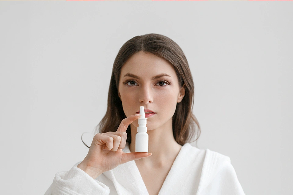 Woman holding a nasal spray bottle, preparing to administer medication.
