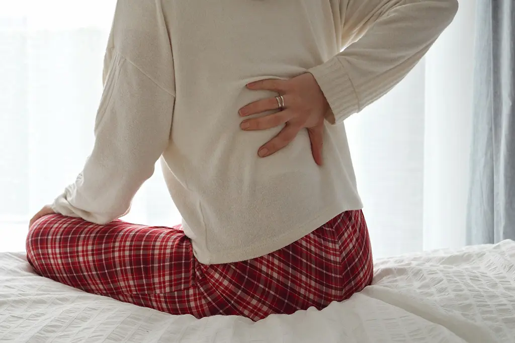 Person in white sweater and red pajama pants clutching their lower back in pain.